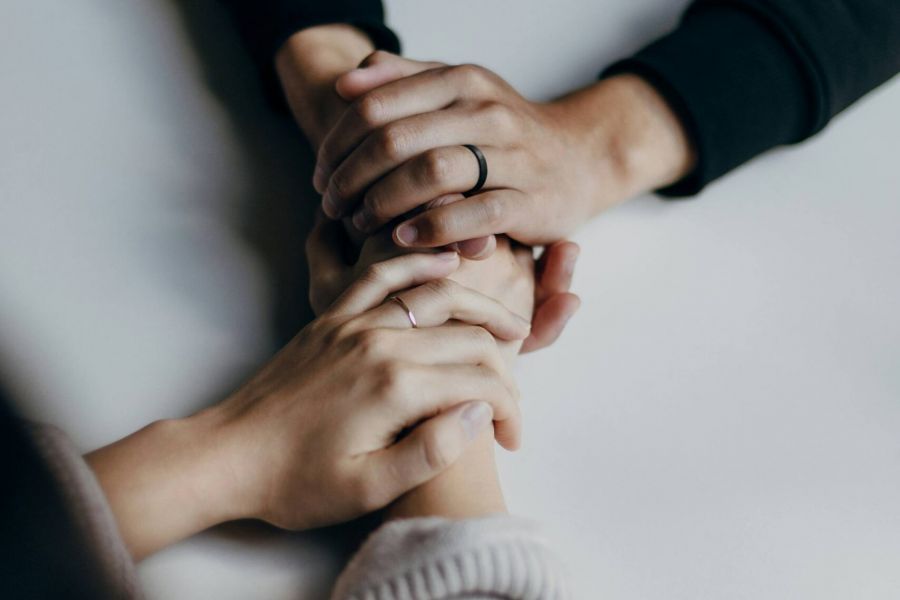 Two people sit across from each other, holding hands in a comforting and supportive gesture on a white surface.